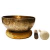 Hammered singing bowl on a gold brocade ring cushion beside a wooden striker and a padded mallet