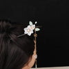 Dark wooden hairpin with white flowers, green leaves and a long gold-tone tassel in a woman's hair bun