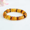Bracelet of honey-yellow and dark red amber disc beads on a white surface, with pink blossoms behind
