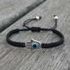 Black braided cord bracelet with a silver hamsa hand and blue evil eye