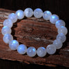 Bracelet of round white moonstone beads with a blue sheen resting on rough tree bark