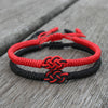 Red and black braided cord bracelets, each with a double coin knot, on a weathered wooden surface