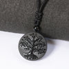 Round black obsidian pendant carved with a tree of life, branches and roots, on a braided black cord