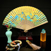 Open folding fan with a blue-green mountain landscape and calligraphy on a yellow leaf, set on a wooden stand