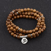 Coiled wooden bead mala bracelet with silver spacers and an Om charm on a dark background