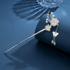 Silver-tone hairpin topped with white plum blossoms, small white buds and a butterfly tassel on a blue backdrop