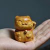 Small carved wooden lucky cat with one paw raised and a bell on a red cord, resting in an open palm