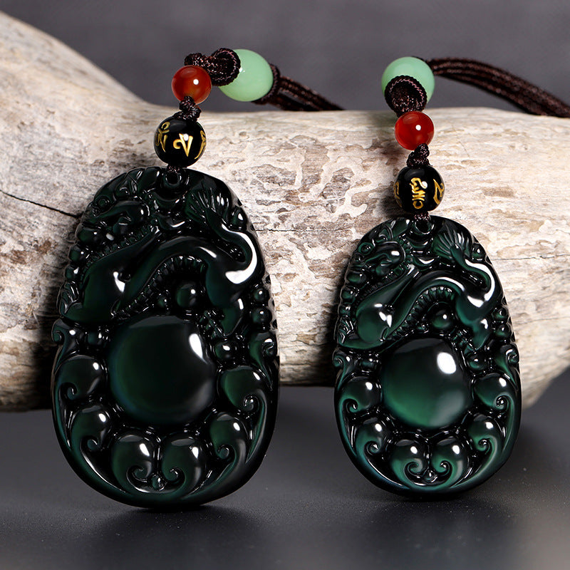 Two black obsidian pendants carved with dragons and holding a sphere, resting on wood.