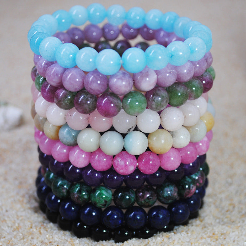 A stack of colorful round stone bead bracelets resting on sand.