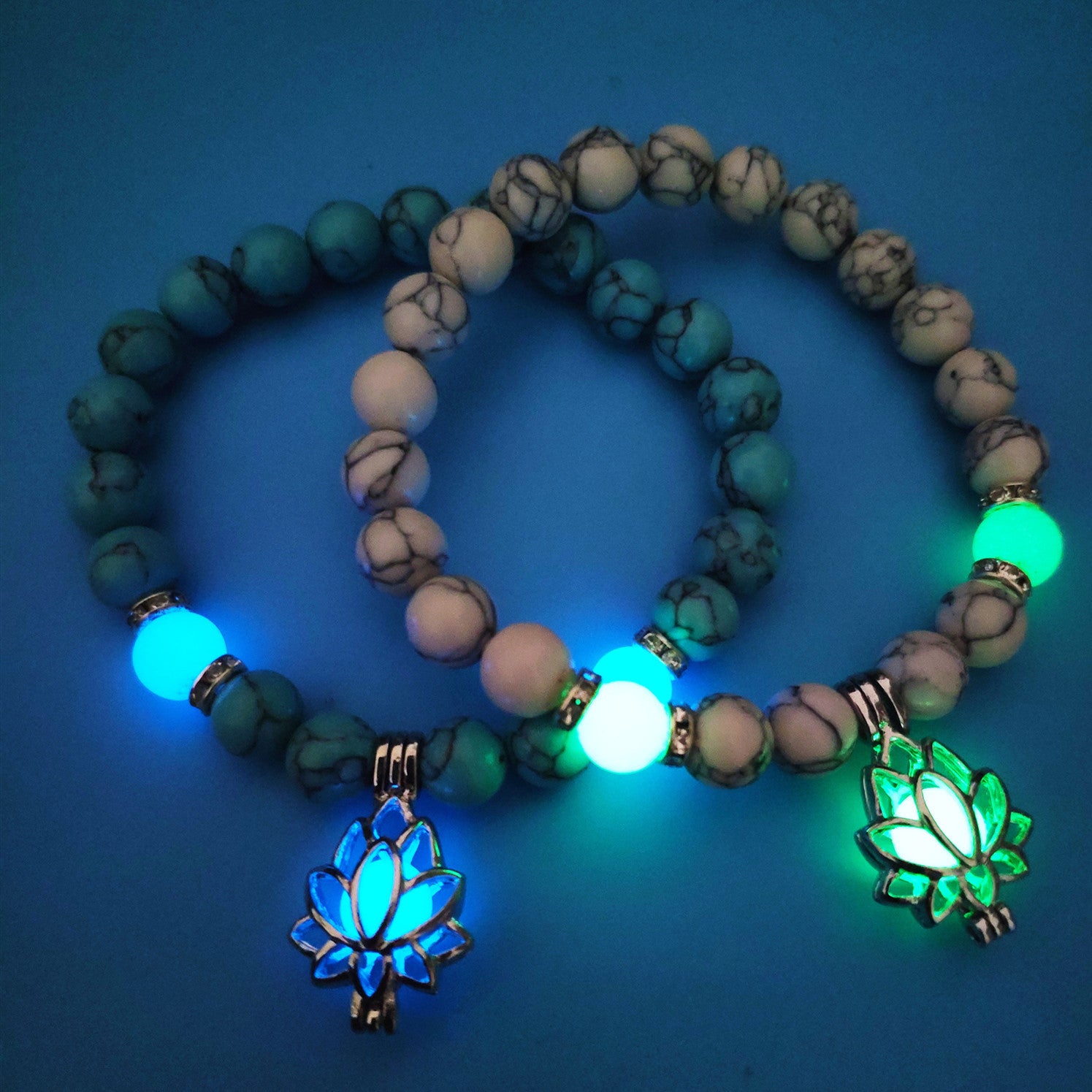 Two bracelets with glowing blue and green lotus charms and beads displayed on a dark background