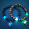 Two bracelets with glowing blue and green lotus charms and beads displayed on a dark background