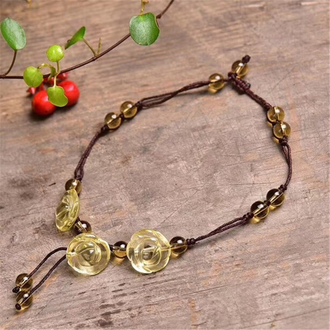 Yellow citrine crystal rose anklet with brown cord lying on wood