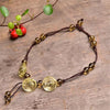 Yellow citrine crystal rose anklet with brown cord lying on wood