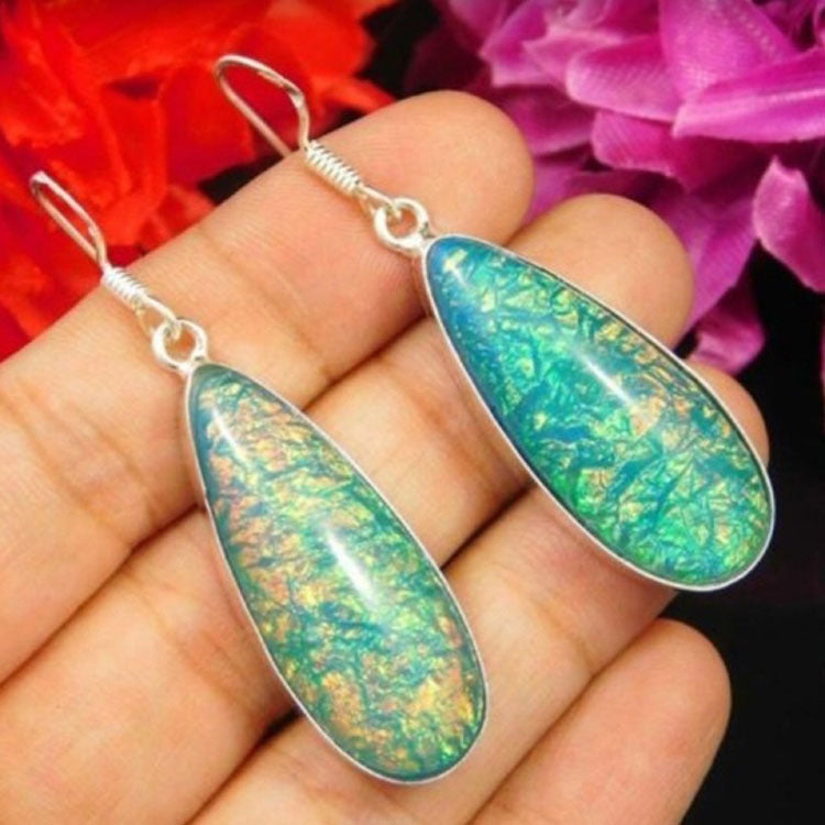 Pair of alloy dangle earrings with green iridescent teardrop stones held in hand