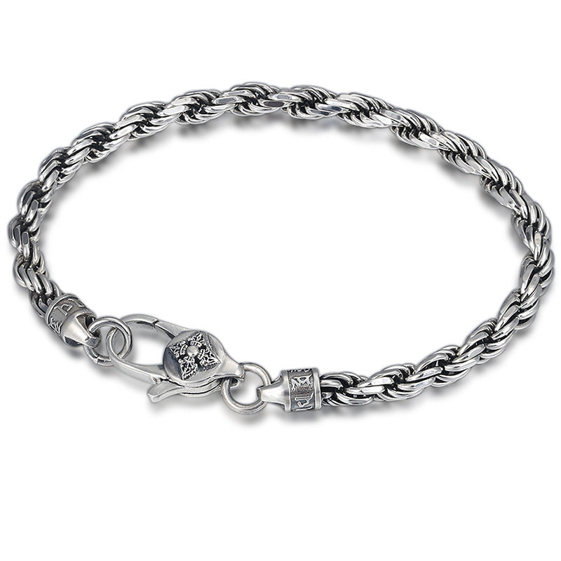 Close up of a twisted sterling silver bracelet with a lobster clasp and vajra charm on a dark surface