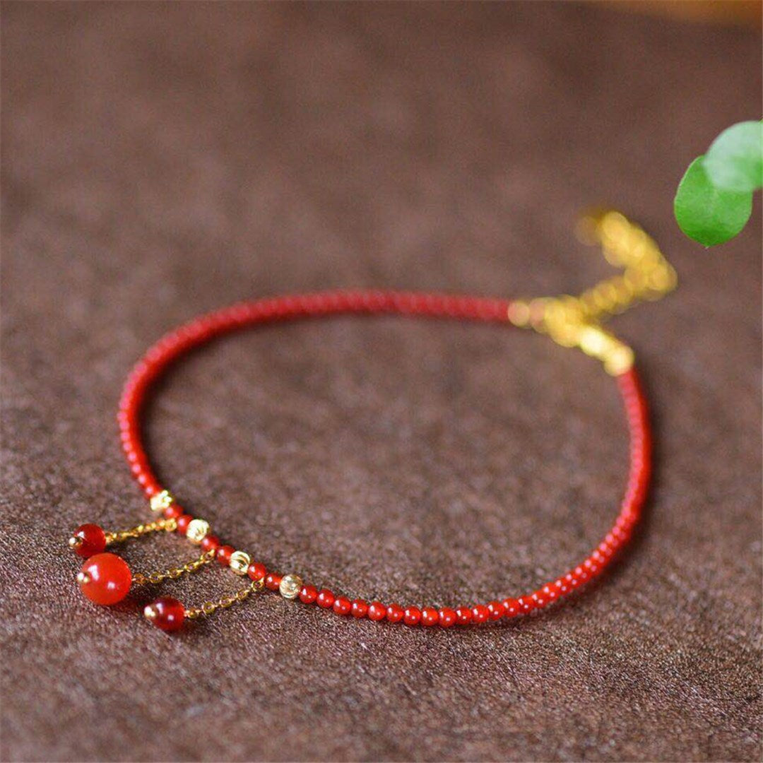 Close up of a red agate beaded anklet with gold tone tassel charms on a brown surface