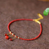 Close up of a red agate beaded anklet with gold tone tassel charms on a brown surface