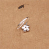 Close up of a silver ring with a small pink flower charm on a brown background
