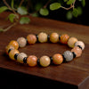 Close up of a Golden Silk Jade bracelet with carved lotus beads and black spacers on a wooden surface