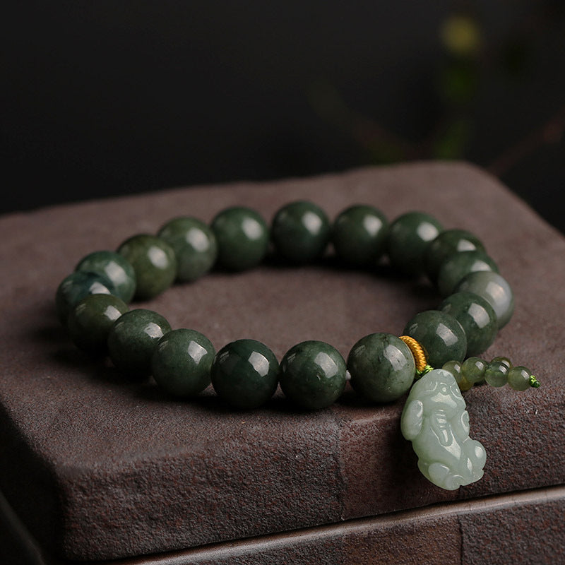 Green jade beaded bracelet with a carved Pixiu charm resting on a wooden surface.