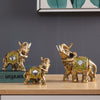 Gold and green resin elephant statue with raised trunk on a wooden surface