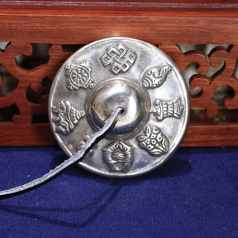 Close up of a silver colored Tibetan tingsha bell with embossed auspicious symbols
