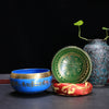 Blue and green Tibetan singing bowls with gold script on a dark table