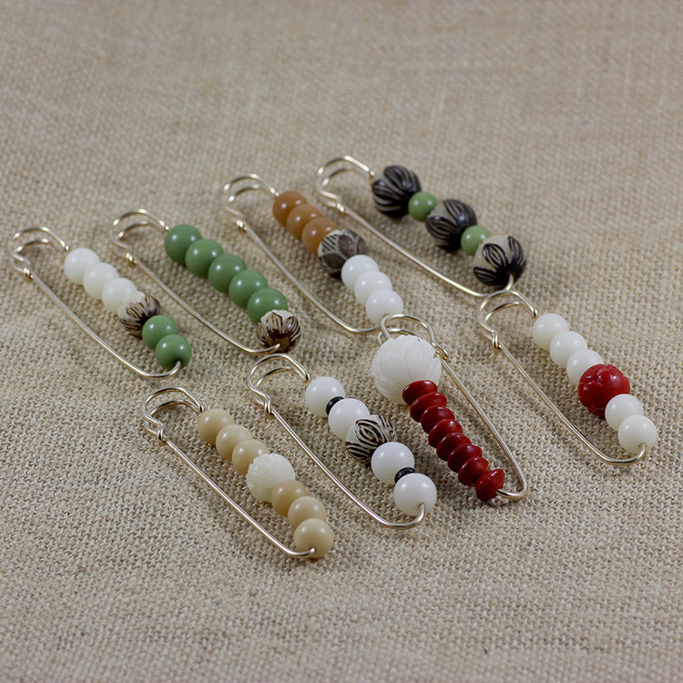 Collection of beaded safety pin brooches with bodhi seeds and colored beads on linen fabric