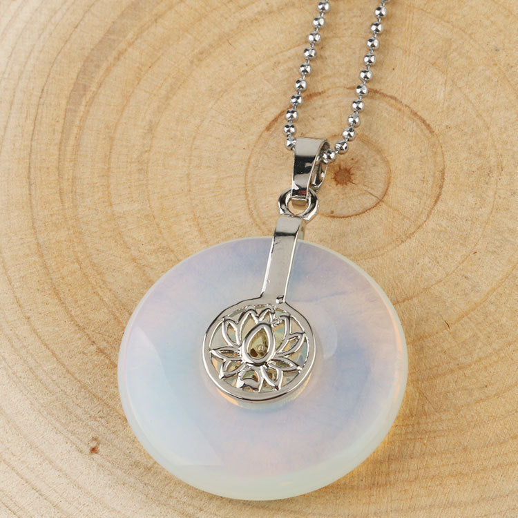 A white opal crystal pendant with a silver lotus charm on a wooden surface