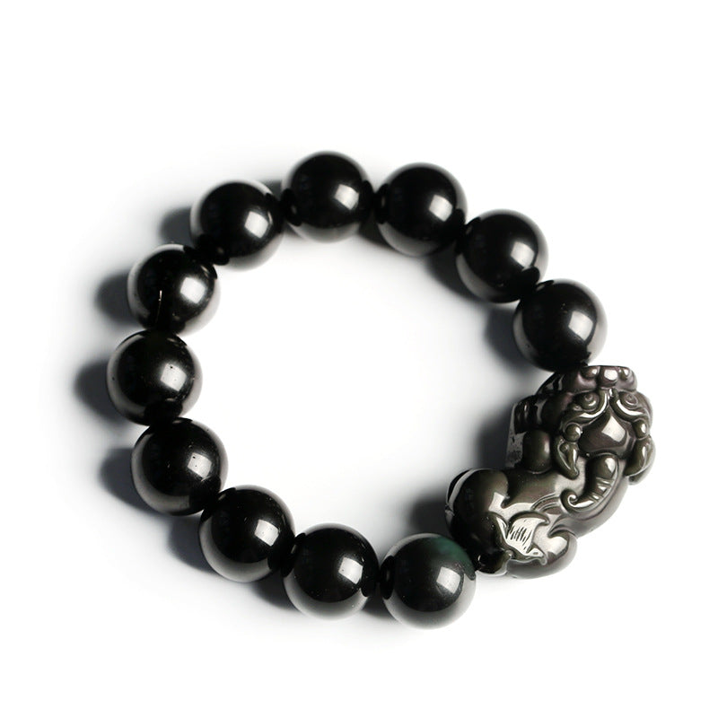 Close up of black obsidian beaded bracelet with carved Pixiu charm on white plate
