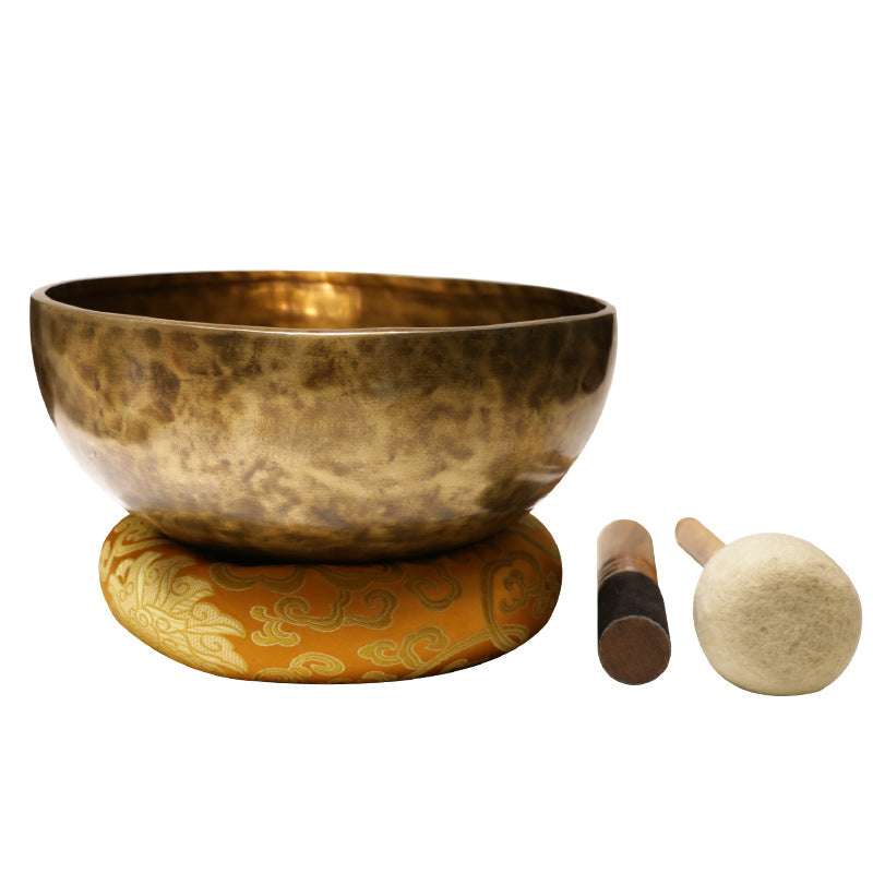 A person holding a handcrafted copper singing bowl while striking it with a mallet.