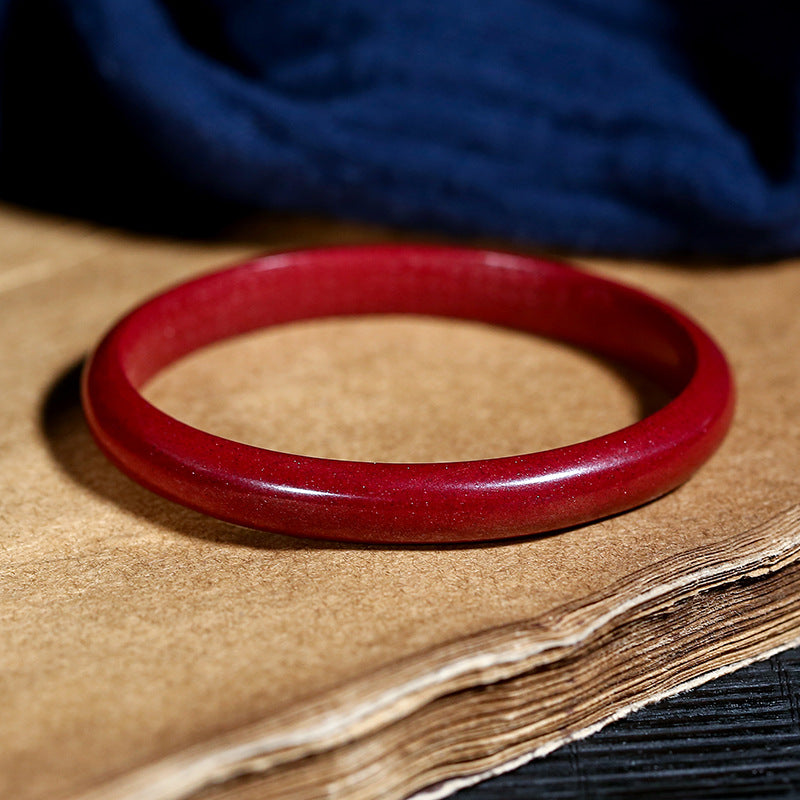 Close up of a polished red cinnabar bangle resting on a textured paper surface.
