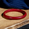 Close up of a polished red cinnabar bangle resting on a textured paper surface.