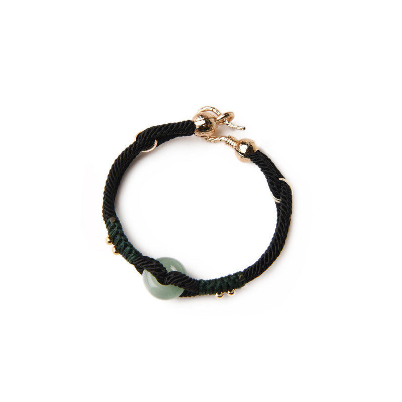 Two people wearing matching black rope bracelets with green stones holding hands outdoors.
