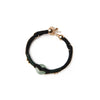 Two people wearing matching black rope bracelets with green stones holding hands outdoors.