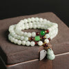 Three-wrap natural jade bracelet with garnet accents and hanging charms on a wooden surface