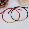Two braided string bracelets, one red and one black, with gold-tone copper beads lying on a white surface.