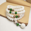 Coiled white bodhi seed mala beads with green accents resting on an open book