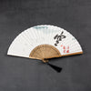 Open white folding fan with bamboo ribs and black calligraphy on a dark background