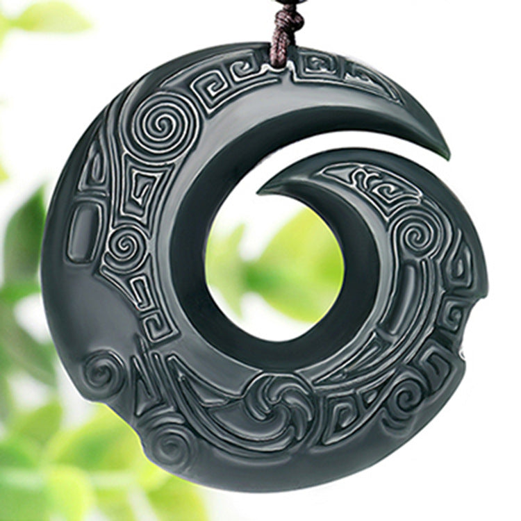 Close up view of dark green carved jade pendant with spiral designs