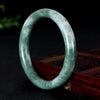 Polished green and white natural jade bangle bracelet standing on a wooden surface