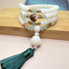 White bodhi seed mala bracelet wrapped on a wooden block with a green tassel