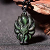 Carved black obsidian fox pendant showing green iridescence on a dark surface
