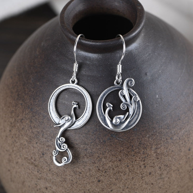 Pair of 925 sterling silver earrings with asymmetrical phoenix design on a dark vase