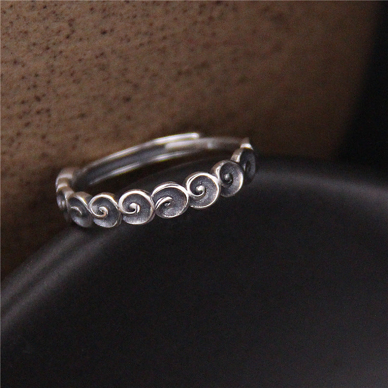 Close up view of a silver ring with a spiral cloud pattern on a dark surface
