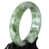 Close up of a green and white Xiuyan jade bangle on a black stand