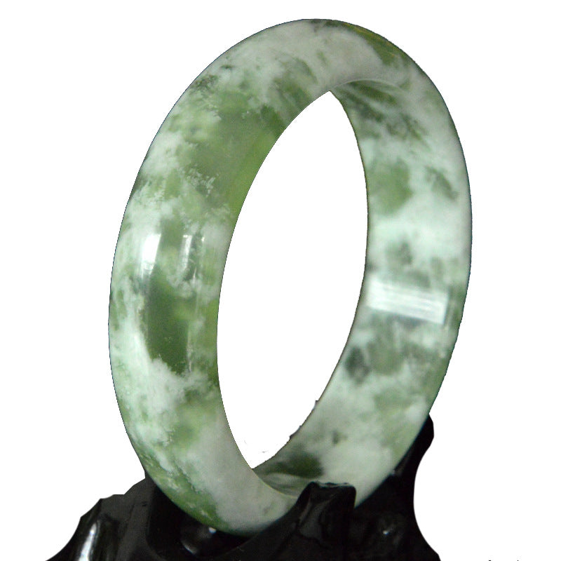 Close up of a green and white Xiuyan jade bangle on a black stand