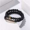 Stacked black frosted and lava rock bracelets with a gold crown charm on a white surface