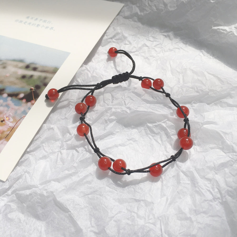 Close up of a red agate bead bracelet with a black cord lying on white paper.