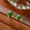 Close up of small round green jade stud earrings with gold rim on wood background